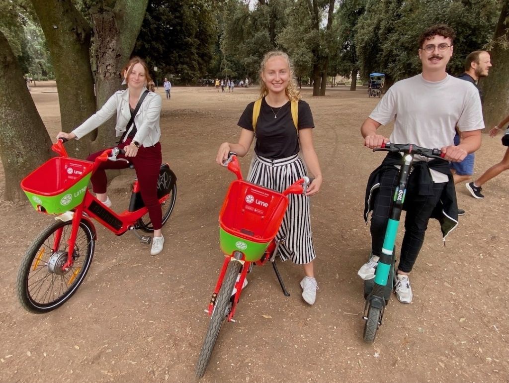 2 filles sur des vélos rouges et verts et un homme sur une trottinette électrique